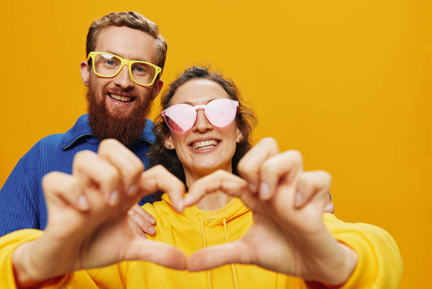 Férfi és nő pár vidáman mosolyog és görbe szemüveggel, sárga háttérrel, szimbólumok és kézmozdulatok, családi fotózás, friss házasok. Kiváló minőségű fénykép - Fotó, kép
