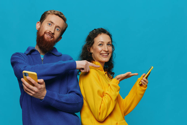 Vrouw en man vrolijk paar met telefoons in hun handen scheef glimlach vrolijk, op blauwe achtergrond. Het concept van echte familierelaties, telefoneren, online werken. Hoge kwaliteit foto - Foto, afbeelding