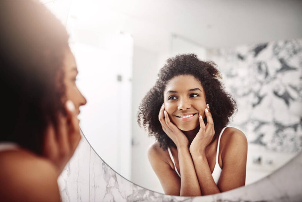 ホテルのウェルネスのためのバスルームで笑顔で鏡の中の女性、スキンケアと皮膚科。モデル、幸せと肌の美しさ、健康的な顔のためのアパートで朝のセルフケアのための輝き - 写真・画像