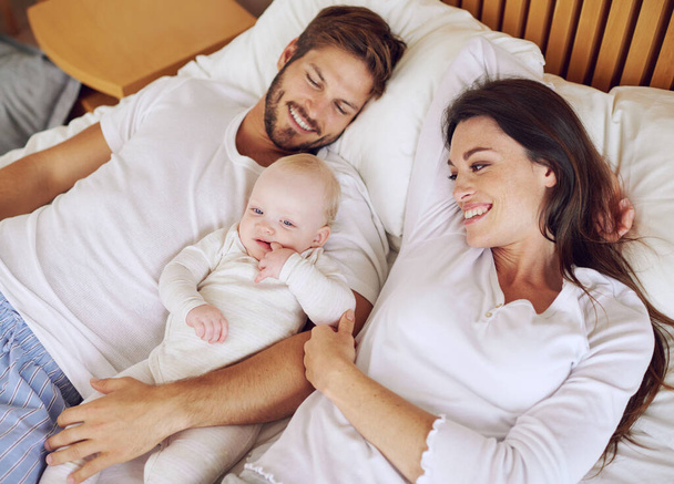 Top view of mother, father and baby on bed for love, care and quality time together. Happy parents, family and newborn kid relaxing in bedroom with support, childhood development and bonding at home. - Zdjęcie, obraz