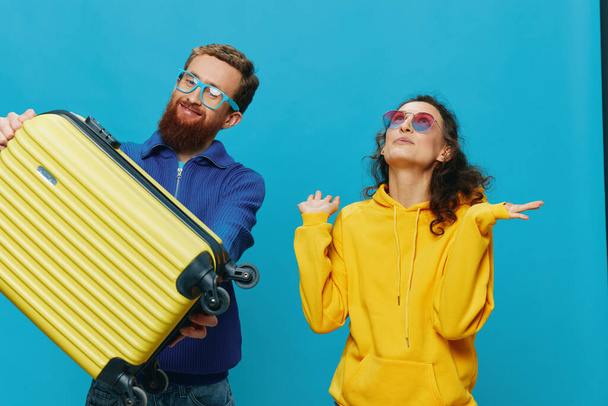 Donna e uomo sorridono seduti sulla valigia con un sorriso giallo valigia, su sfondo blu, imballaggio per il viaggio, viaggio di vacanza in famiglia. Foto di alta qualità - Foto, immagini