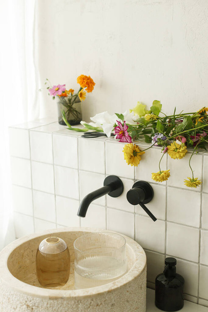 Beautiful flowers bouquet in modern marble sink in stylish bathroom. Summer flowers arrangement gathered from garden in modern room in home - Fotografie, Obrázek