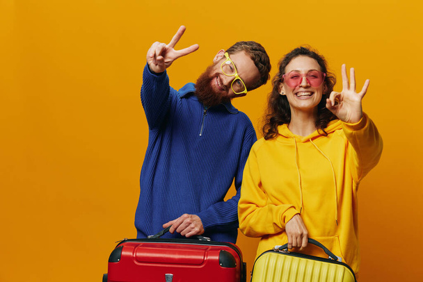 Женщина и мужчина улыбаются, чемоданы в руке с желтым и красным чемоданом весело и криво улыбаются, желтый фон, отправляются в путешествие, семейный отдых, молодожены. Высокое качество фото - Фото, изображение