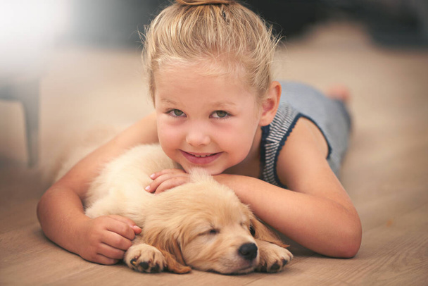 Dívka obejmout své štěně na portrét, relaxovat doma a šťastný se spaním zlatý retrívr a dítě s úsměvem. Štěstí, péče o domácí mazlíčky a láska k ženskému dítěti s domácím zvířetem ležícím na dřevěné podlaze. - Fotografie, Obrázek
