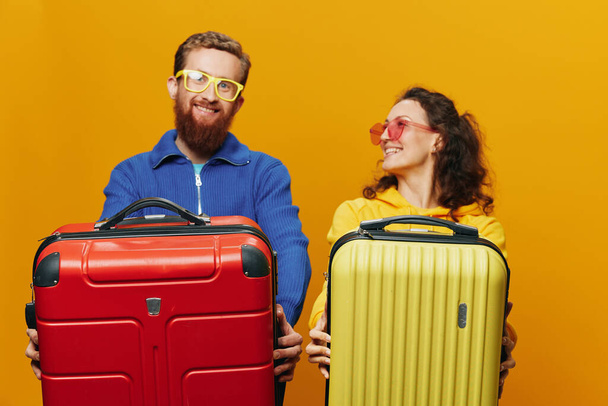 Vrouw en man glimlachend, koffers in de hand met gele en rode koffer lachend vrolijk en scheef, gele achtergrond, op reis gaan, familie vakantie reis, pasgetrouwden. Hoge kwaliteit foto - Foto, afbeelding