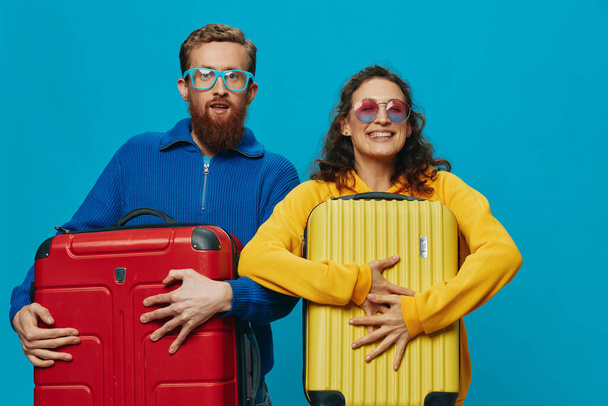 Kobieta i mężczyzna uśmiechają się walizki w dłoni z żółto-czerwoną walizką uśmiech zabawy, na niebieskim tle, pakowanie na wycieczkę, rodzinny wyjazd wakacyjny. Wysokiej jakości zdjęcie - Zdjęcie, obraz