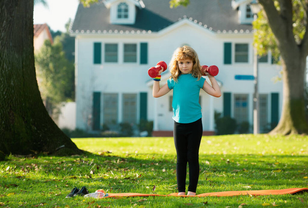Fitness child. Sport activities at leisure with children outdoor. Beautiful blonde boy holding dumbbells in park - Zdjęcie, obraz