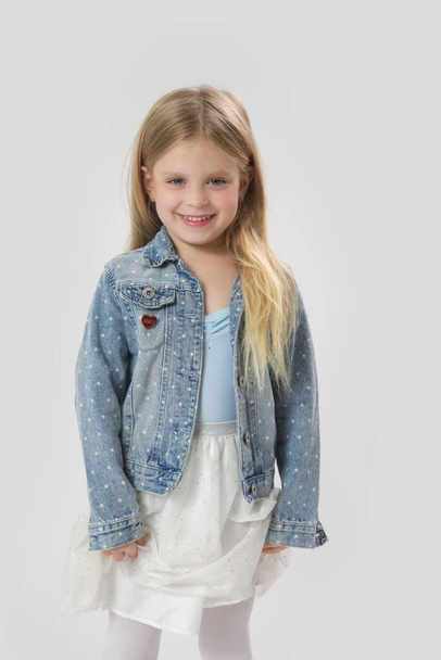 Студийный портрет красивой веселой модной девочки в юбке из пачки и джинсовой куртке на белом фоне - Фото, изображение