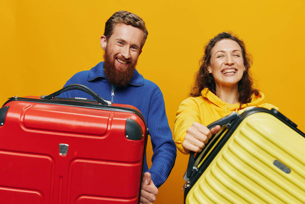Kobieta i mężczyzna uśmiechnięci, walizki w dłoni z żółtą i czerwoną walizką uśmiechnięci wesoło i krzywo, żółte tło, wyjazd w podróż, rodzinne wakacje, nowożeńcy. Wysokiej jakości zdjęcie - Zdjęcie, obraz
