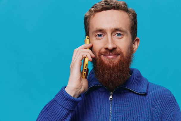 Portrait of a man with a phone in his hands talking, calling, on a blue background. Communicating online social media, lifestyle. High quality photo - Photo, Image