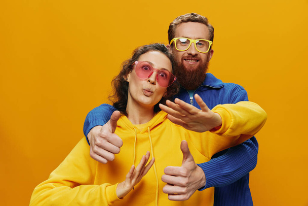 Man and woman couple smiling cheerfully and crooked with glasses, on yellow background, symbols signs and hand gestures, family shoot, newlyweds. High quality photo - Valokuva, kuva