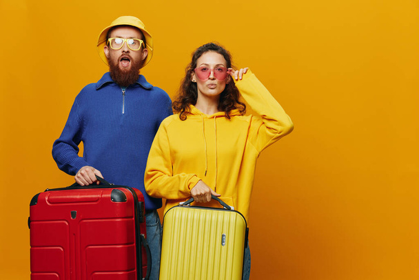 Nő és férfi mosolyog, bőröndök a kezükben sárga és piros bőrönddel, vidám és görbe mosollyal, sárga háttér, kirándulás, családi nyaralás, friss házasok. Kiváló minőségű fénykép - Fotó, kép