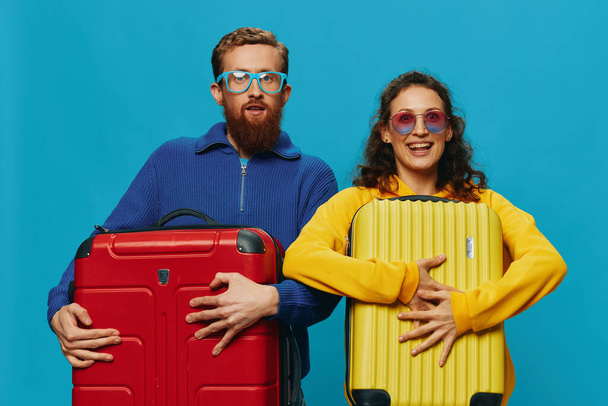 Mujer y hombre sonríen maletas en la mano con amarillo y rojo maleta sonrisa diversión, sobre fondo azul, embalaje para un viaje, viaje de vacaciones familiares. Foto de alta calidad - Foto, imagen