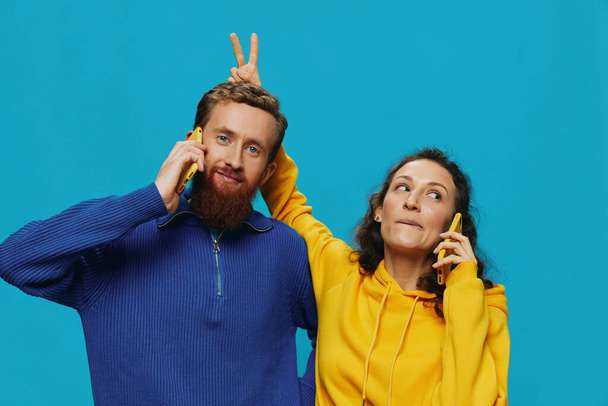 Γυναίκα και άνθρωπος χαρούμενο ζευγάρι με τηλέφωνα στα χέρια τους στραβό χαμόγελο χαρούμενο, σε μπλε φόντο. Η έννοια των πραγματικών οικογενειακών σχέσεων, μιλάμε στο τηλέφωνο, εργάζονται σε απευθείας σύνδεση. Υψηλής ποιότητας φωτογραφία - Φωτογραφία, εικόνα