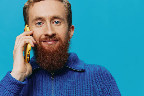 Portrait of a man with a phone in his hands talking, calling, on a blue background. Communicating online social media, lifestyle. High quality photo - Photo, Image