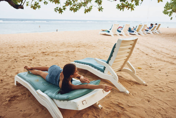 attrayant femme océan station balnéaire mode de vie de la mer chaise de relaxation jeune repos sable tropical couché souriant soleil bleu transat plage chapeau vacances - Photo, image