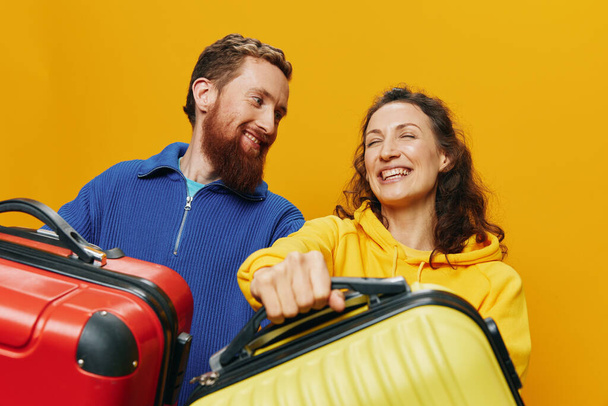 Kadın ve erkek gülümsüyor, ellerinde sarı ve kırmızı bavullar neşeyle ve çarpık bir şekilde gülümsüyor, sarı arka plan, seyahate çıkıyor, aile tatili, yeni evliler. Yüksek kalite fotoğraf - Fotoğraf, Görsel