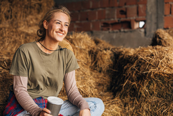 A beautiful happy woman sitting on the haystack and looking away - Φωτογραφία, εικόνα