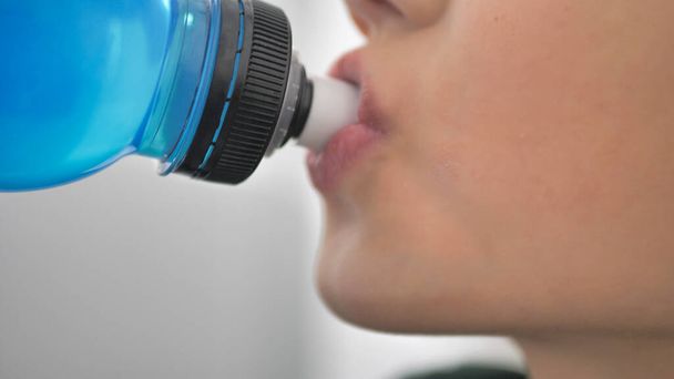 Taking a break. Side view of sporty teenager drinking blue energy drink. Youth and sports. - Foto, Imagem