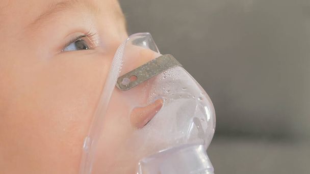 Gros plan du petit garçon est traité problème respiratoire avec nébuliseur de vapeur pour soulager les symptômes de toux dans la chambre d'hôpital, concept de soins pédiatriques pour les patients malades à l'hôpital - Photo, image
