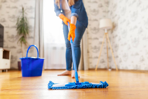 Καλλιεργημένη εικόνα νεαρής γυναίκας με casual ρούχα να πλένει ένα ξύλινο πάτωμα με μια υγρή σφουγγαρίστρα μικροϊνών, να κάνει κατ 'οίκον εργασία, τακτικός καθαρισμός, έννοια εργασιών καθαρισμού - Φωτογραφία, εικόνα