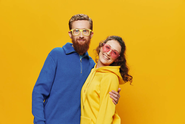 Άνδρας και γυναίκα ζευγάρι χαμογελά χαρούμενα και στραβά με γυαλιά, σε κίτρινο φόντο, σύμβολα σημάδια και χειρονομίες, οικογενειακή φωτογράφιση, νεόνυμφοι. Υψηλής ποιότητας φωτογραφία - Φωτογραφία, εικόνα