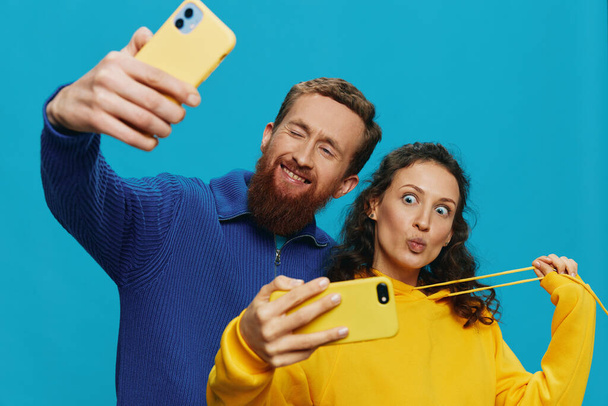 Woman and man funny couple with phones in hand taking selfies crooked smile fun, on blue background. The concept of real family relationships, talking on the phone, work online. High quality photo - Photo, Image