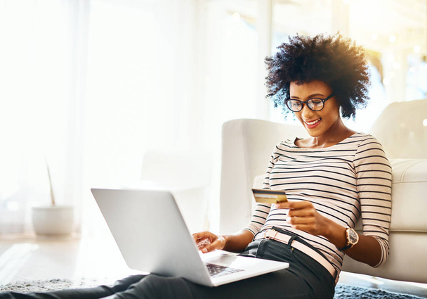 Young woman, laptop and credit card while doing online shopping sitting on ground. Home, happiness and computer internet deal of African female person on an ecommerce app reading banking details. - Фото, зображення