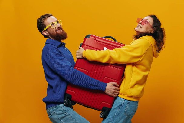 Жінка і чоловік посміхаються, валізи в руці з жовтим і червоним валізою усміхаються весело і криво, жовтий фон, йдуть у подорож, сімейні канікули, молодята. Високоякісна фотографія - Фото, зображення