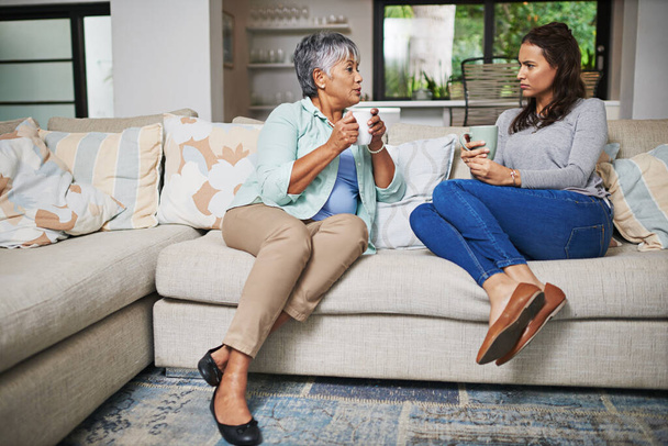 Support, coffee and mother with daughter on sofa in living room for bonding, conversation and free time. Relax, chat and discussion with women talking in family home for generations, reunion or break. - Foto, afbeelding