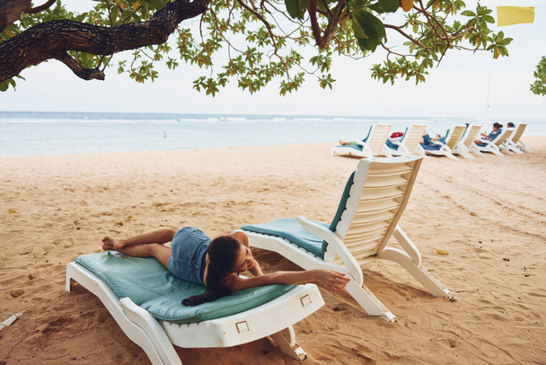 女性の海のビーチ注意深い砂浜の夏の笑顔の太陽の魅力は美しい女性の海のライフスタイル青い椅子の帽子のリゾートの椅子を横たえています - 写真・画像