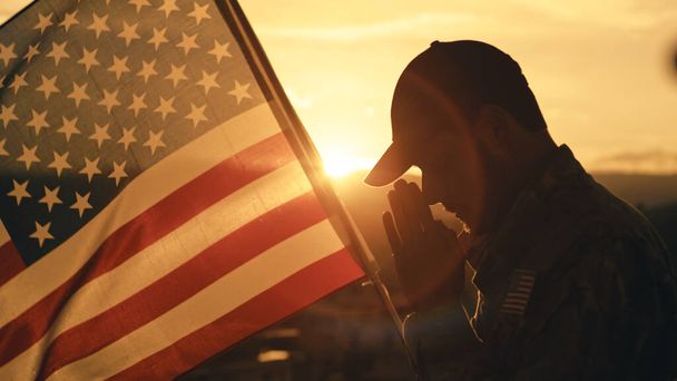 Silueta del soldado americano rezando por el día conmemorativo contra la bandera al aire libre. - Foto, imagen