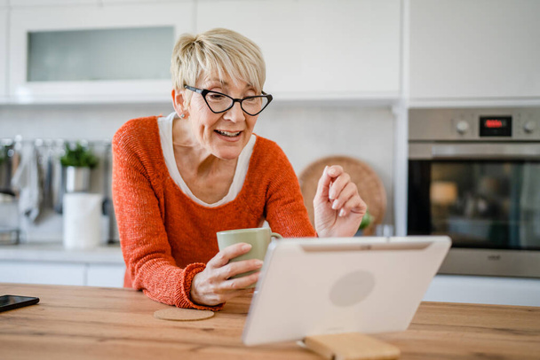 μία γυναίκα ώριμη ξανθιά καυκάσια ηλικιωμένη γυναίκα στο σπίτι χρησιμοποιούν ψηφιακή ταμπλέτα για βιντεοκλήση σε απευθείας σύνδεση συνομιλία στο διαδίκτυο ομιλία στο app πραγματικό πρόσωπο αντίγραφο χώρο - Φωτογραφία, εικόνα