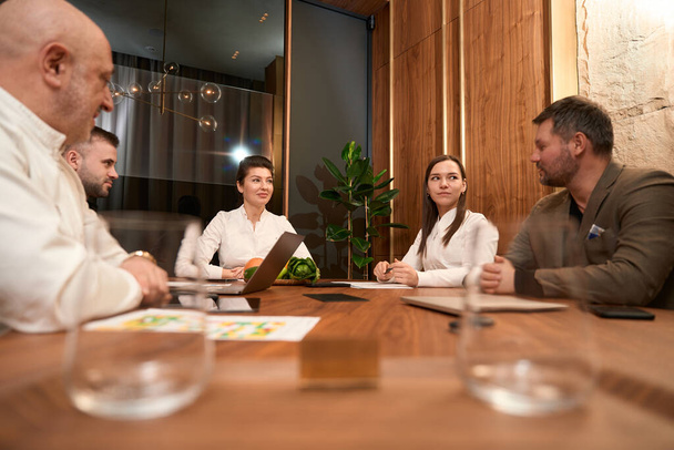 Skupina lékařů sedí u stolu a dívá se na dospělého muže v kanceláři - Fotografie, Obrázek