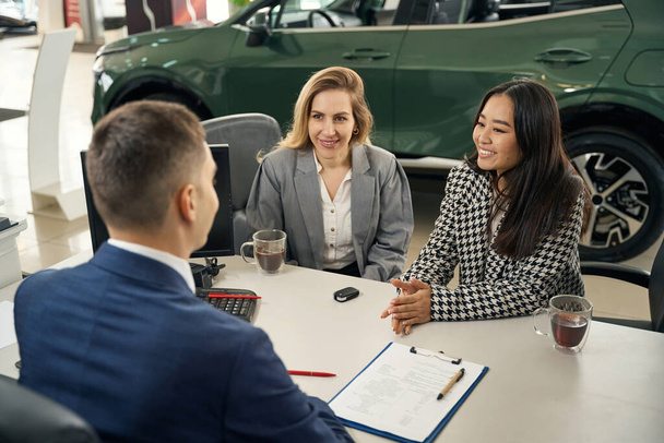 Cute female LGBT couple and a man in the office area of car dealership, partners arrange loan - Photo, Image
