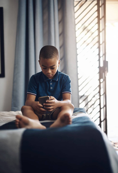 Изучение новых слов онлайн. мальчик пользуется мобильным телефоном, сидя на кровати - Фото, изображение
