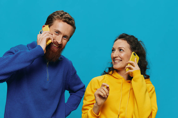 Frau und Mann fröhliches Paar mit Telefonen in den Händen, schiefes Lächeln fröhlich, auf blauem Hintergrund. Das Konzept echter Familienbeziehungen, das Telefonieren, funktioniert online. Hochwertiges Foto - Foto, Bild