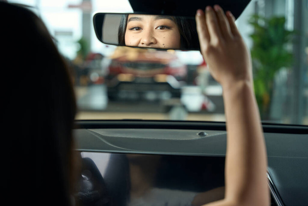Очаровательная молодая женщина сидит за рулем автомобиля, она смотрит в зеркало заднего вида - Фото, изображение