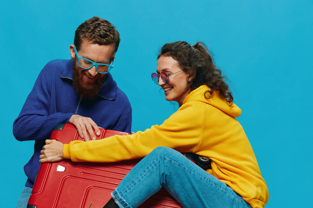 Mulher e homem sorrir malas na mão com amarelo e vermelho mala sorrir diversão, no fundo azul, a embalagem para uma viagem, viagem de férias em família. Foto de alta qualidade - Foto, Imagem