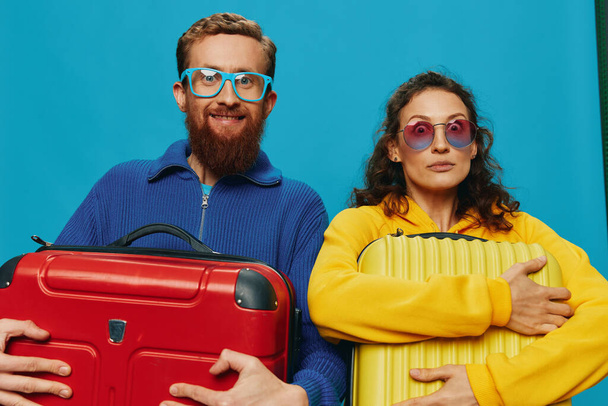 Donna e uomo sorridono valigie in mano con valigia gialla e rossa sorridono divertimento, su sfondo blu, fare i bagagli per un viaggio, viaggio di vacanza in famiglia. Foto di alta qualità - Foto, immagini