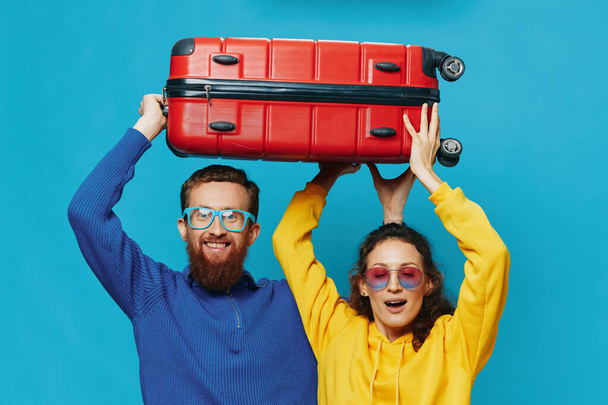 Vrouw en man glimlach koffers in de hand met gele en rode koffer glimlach plezier, op blauwe achtergrond, verpakking voor een reis, familie vakantie reis. Hoge kwaliteit foto - Foto, afbeelding