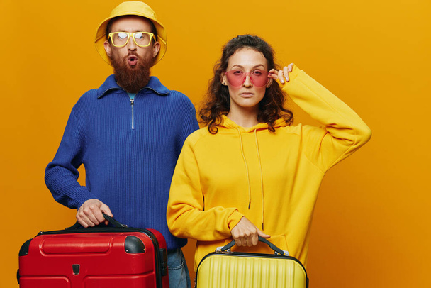 Nainen ja mies hymyilevä, matkalaukut kädessä keltainen ja punainen matkalaukku hymyillen iloisesti ja vino, keltainen tausta, lähdössä matkalle, perheen loma matka, nuoripari. Laadukas kuva - Valokuva, kuva