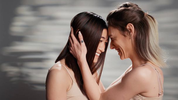 Beautiful natural women sharing hug in studio, feeling confident with bare skin and advertising self confidence. Interracial girls promoting beauty products and routine on camera, self love. - Photo, Image