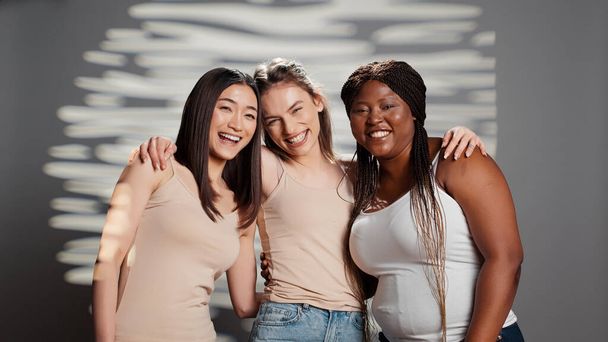 Interracial group of girls with different body types being happy in studio, feeling flawless and advertising bodycare campaign. Young diverse women smiling on camera and promoting body positivity. - 写真・画像