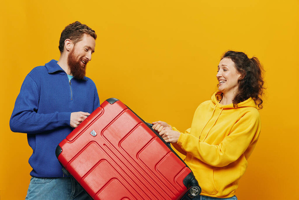 Frau und Mann lächeln, Koffer in der Hand mit gelb-rotem Koffer, fröhlich und schief lächelnd, gelber Hintergrund, auf Reisen, Familienurlaub, Brautpaar. Hochwertiges Foto - Foto, Bild