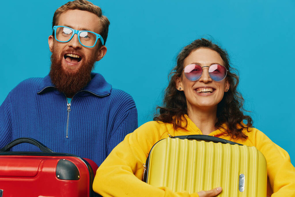Mujer y hombre sonríen maletas en la mano con amarillo y rojo maleta sonrisa diversión, sobre fondo azul, embalaje para un viaje, viaje de vacaciones familiares. Foto de alta calidad - Foto, Imagen