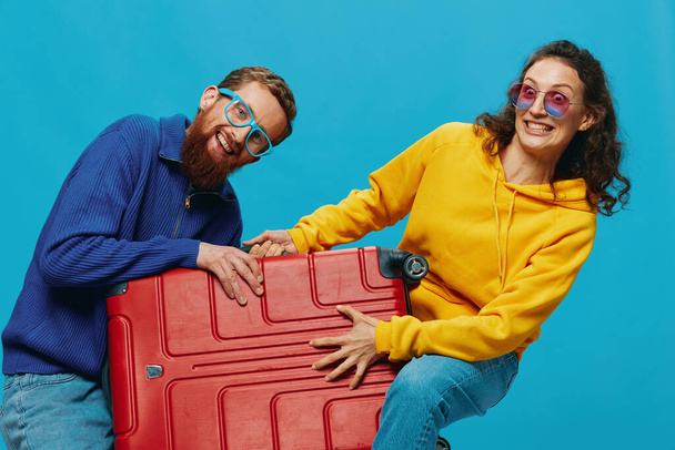 Mujer y hombre sonríen maletas en la mano con amarillo y rojo maleta sonrisa diversión, sobre fondo azul, embalaje para un viaje, viaje de vacaciones familiares. Foto de alta calidad - Foto, Imagen