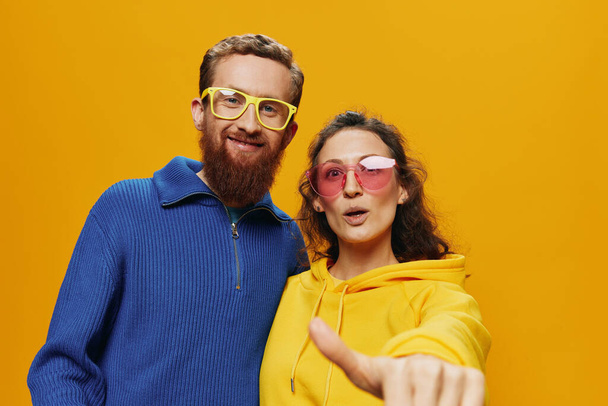 Άνδρας και γυναίκα ζευγάρι χαμογελά χαρούμενα και στραβά με γυαλιά, σε κίτρινο φόντο, σύμβολα σημάδια και χειρονομίες, οικογενειακή φωτογράφιση, νεόνυμφοι. Υψηλής ποιότητας φωτογραφία - Φωτογραφία, εικόνα
