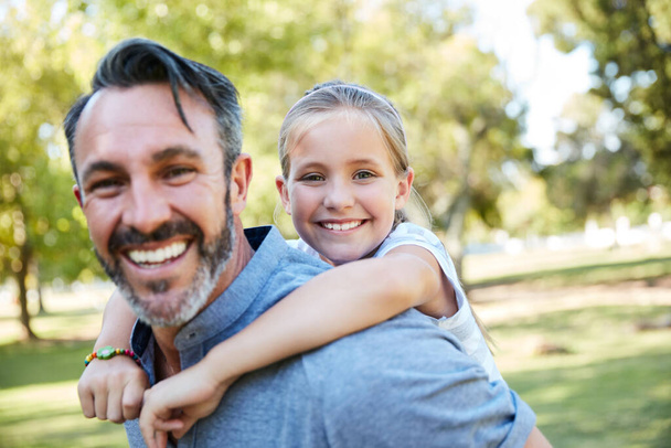 Geef ze wat ze het meest nodig hebben, jouw tijd. een schattig klein meisje genieten van een piggyback rit met haar vader in het park - Foto, afbeelding