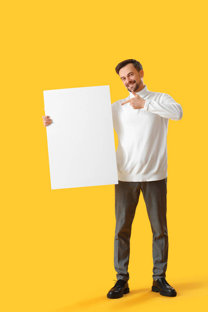 Schöner Mann zeigt auf großes leeres Plakat auf gelbem Hintergrund - Foto, Bild